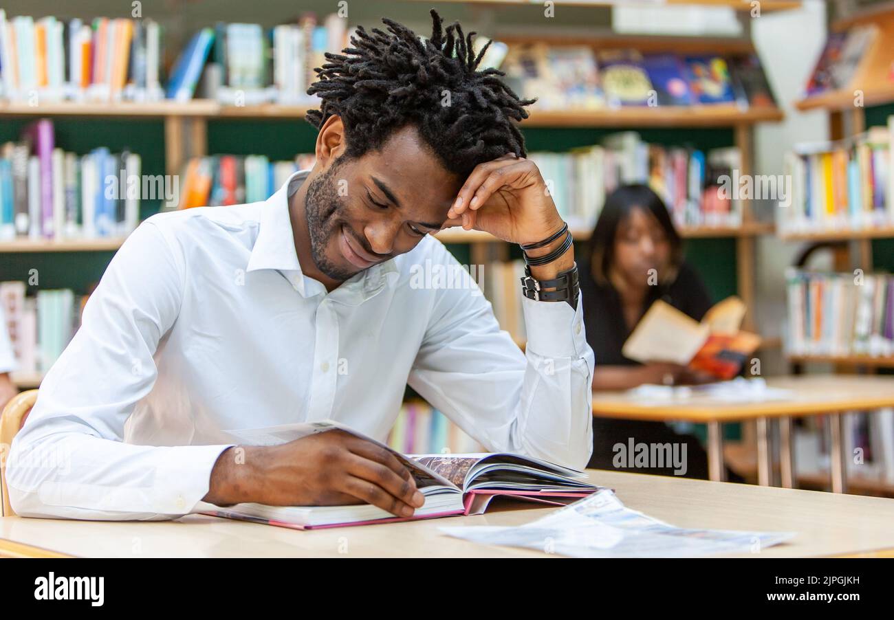 Jugendliche Studenten, akademische Forschung. Ein junger erwachsener Mann, der in einer Bibliothek Nachschlagewerk liest. Aus einer Reihe verwandter Bilder. Stockfoto