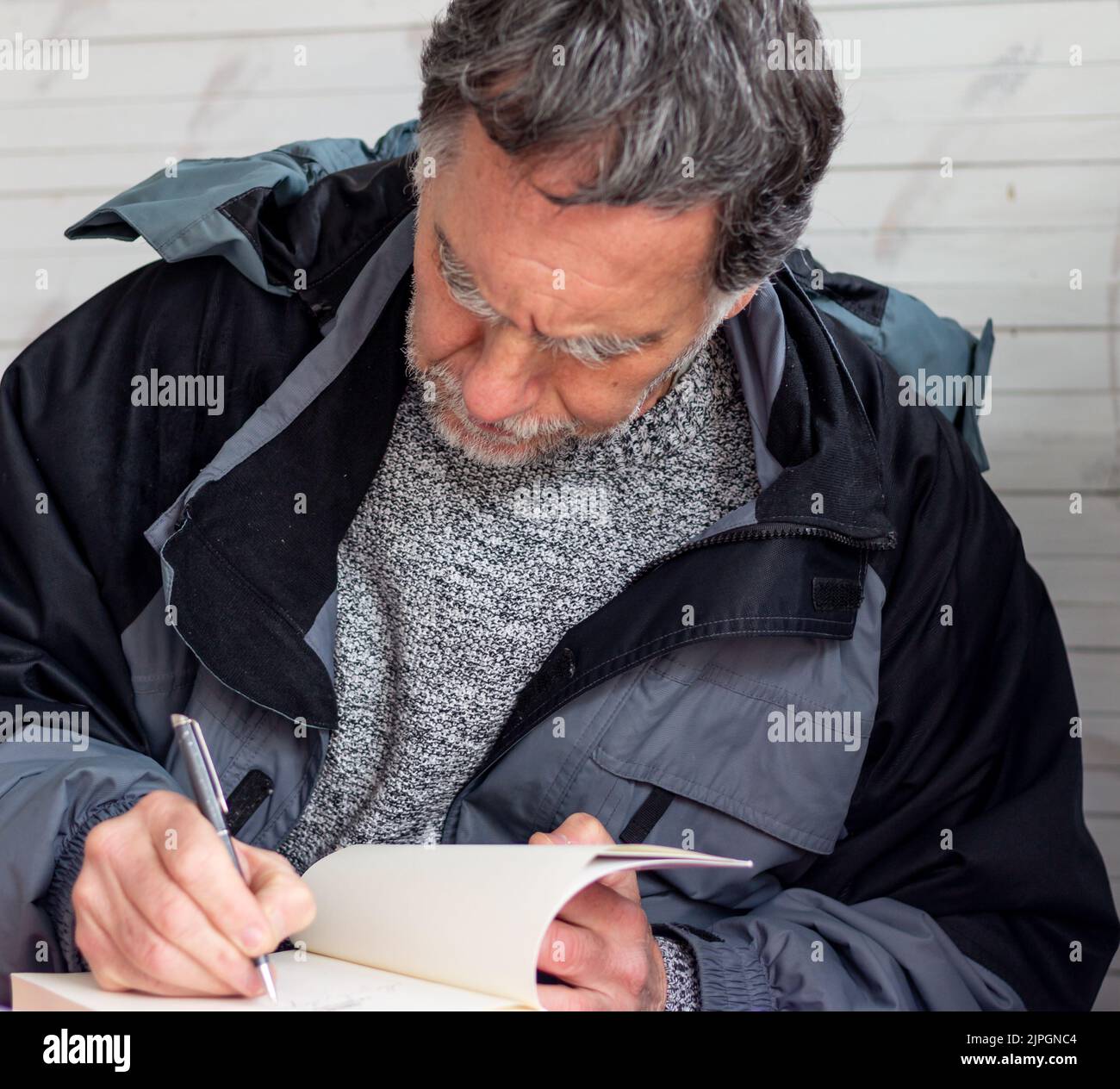 Ein Mann mit Bart und grauen Haaren schreibt ein Buch Stockfoto