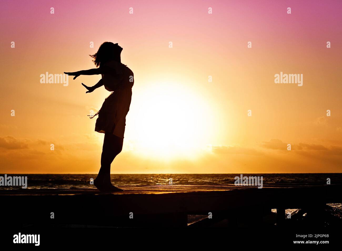 Eine Silhouette eines Mädchens mit weit geöffneten Armen und Blick auf den Sonnenuntergang im Hintergrund Stockfoto