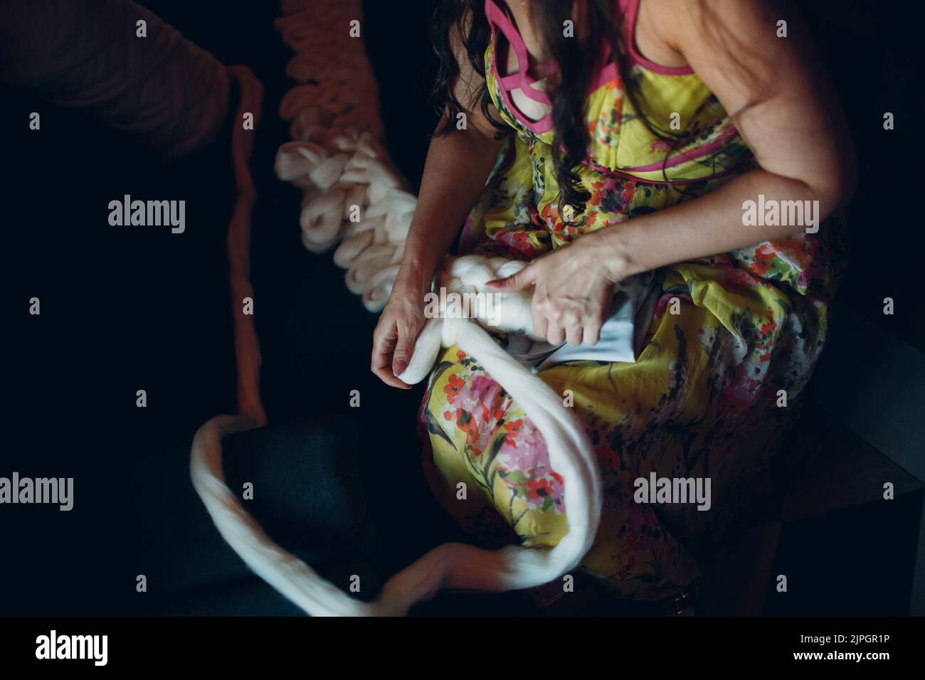 Große Gebärmutter aus dicken Fäden Frau und weißem Garn zum Weben eines Plaid aus Wolle. Stockfoto