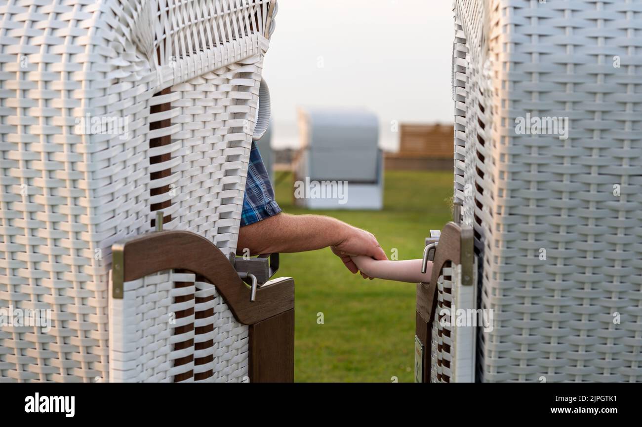 Großvater und Enkelkind halten sich die Hände, während sie in Strandstühlen in Cuxhaven sitzen. Stockfoto