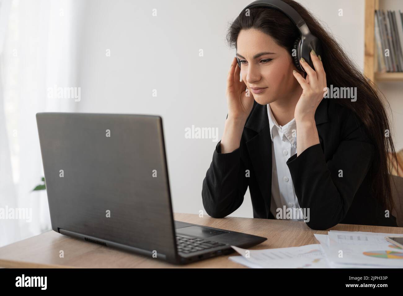 Seriöse Geschäftsfrau mit Kopfhörern, die sich ein Webinar auf dem Laptop ansieht, Computerkurse lernt, Anrufe tätigen, an Online-Konferenzen teilnehmen Stockfoto