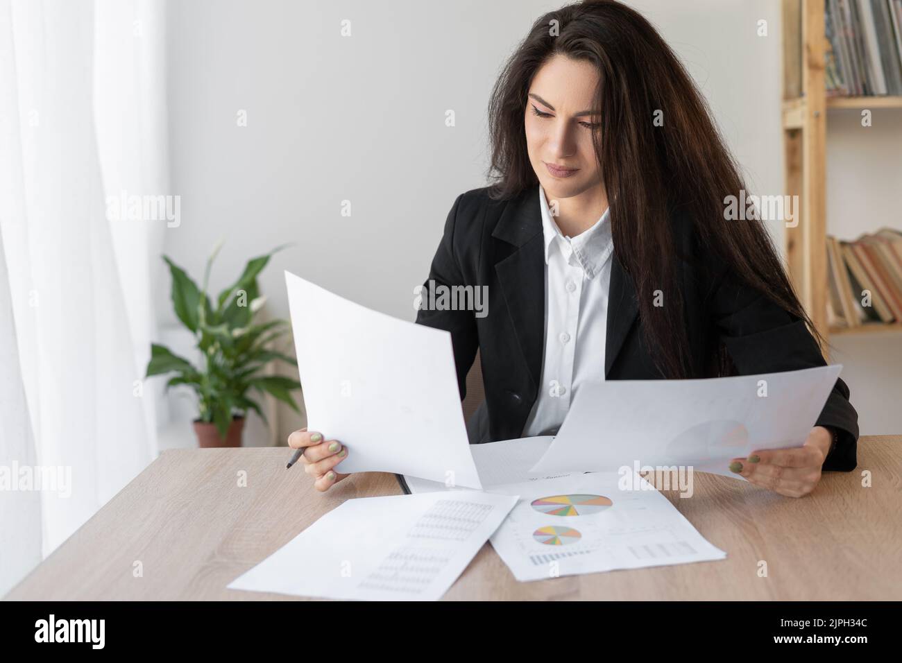 Seriöse lateinische Geschäftsfrau, die im Büro mit Dokumenten arbeitet. Die arbeitenden Frauen arrangieren Dokumente mit Papieren auf dem Schreibtisch Stockfoto