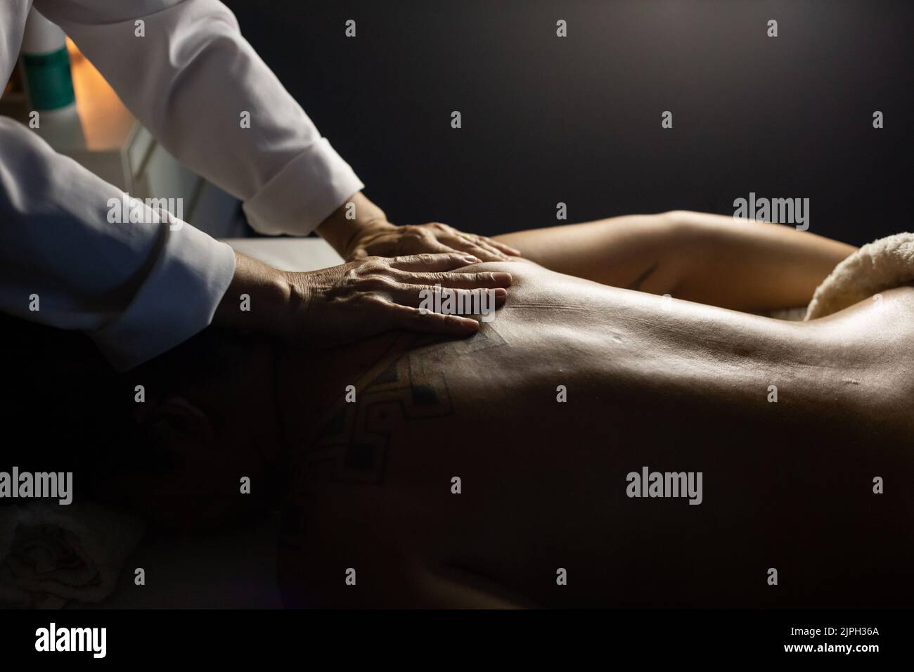 Goiânia, Goias, Brasilien – 18. Juli 2022: Detail eines Massagetherapeuten, der den Rücken eines Patienten massiert, der auf einer Bahre liegt. Dunkler Hintergrund. Stockfoto