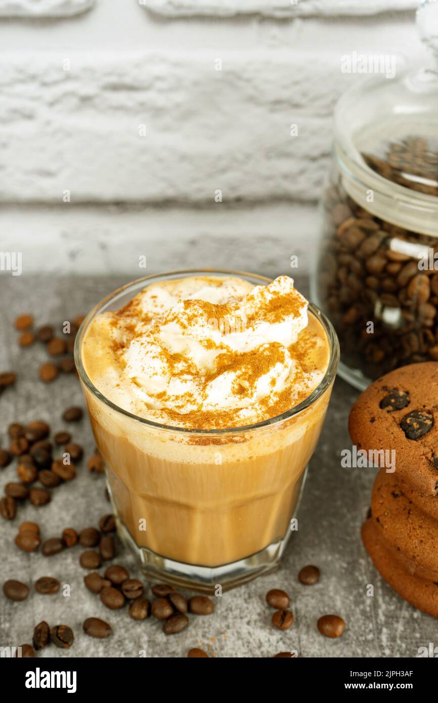 Karamell-Latte-Kaffee in einem Glas mit Schlagsahne und Schokoladenkekse. Kaffeebohnen auf grauer und weißer Ziegelwand mit Kopierfläche. Stockfoto
