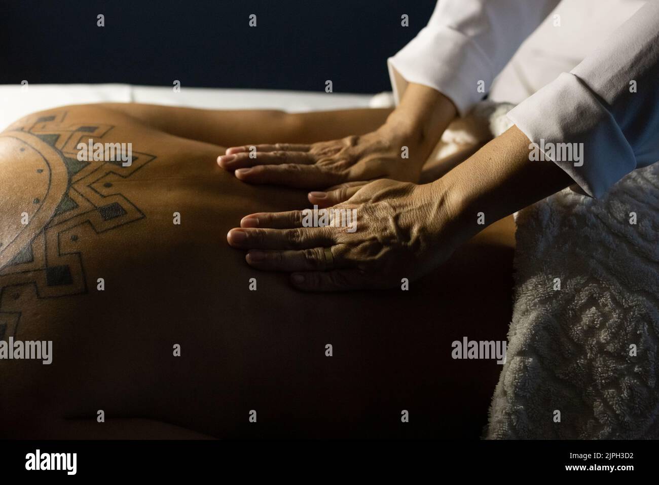 Goiânia, Goias, Brasilien – 18. Juli 2022: Detail eines Massagetherapeuten, der den Rücken eines Patienten massiert, der auf einer Bahre liegt. Dunkler Hintergrund. Stockfoto