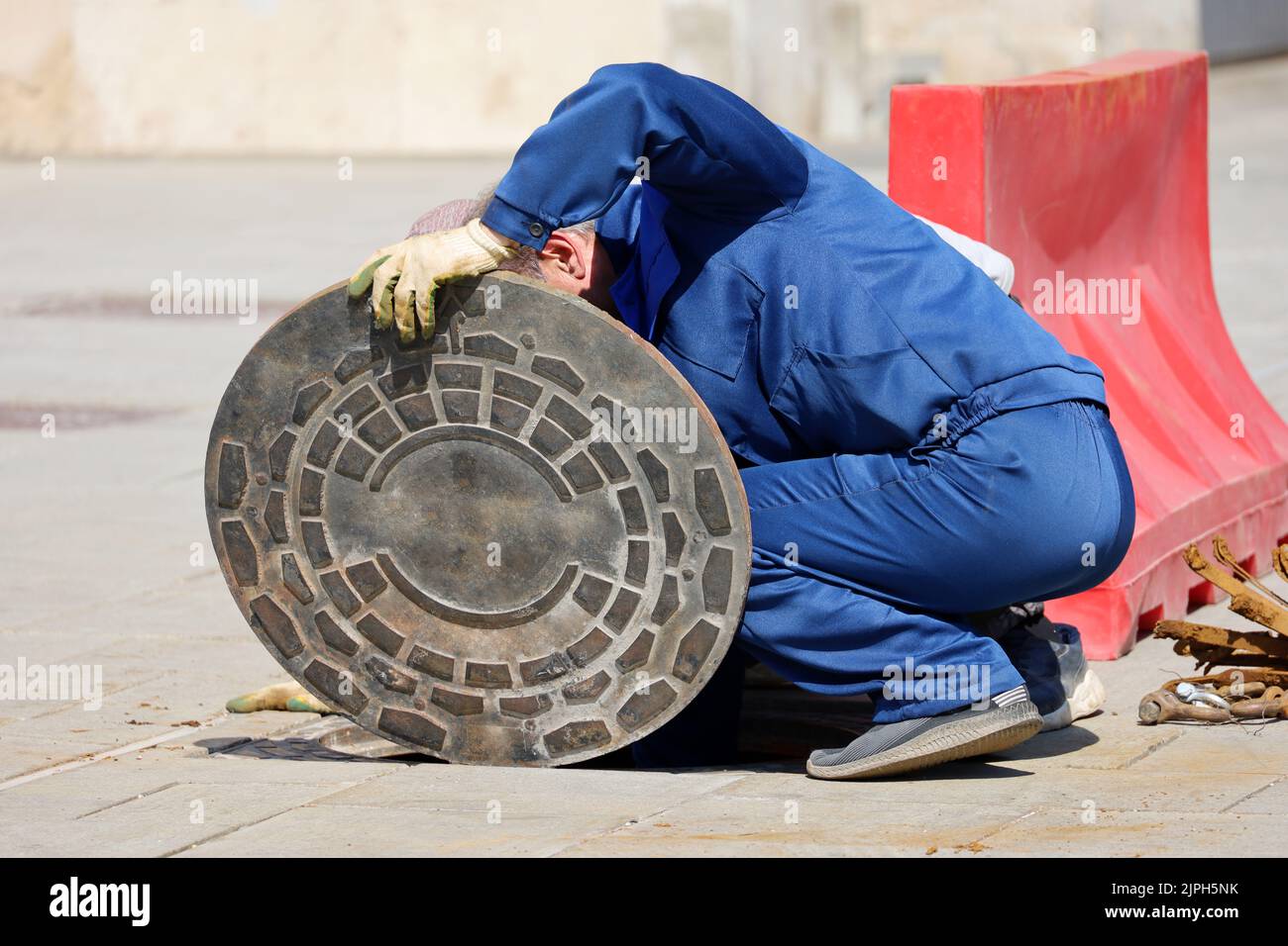 Arbeiter in blauer Uniform über der offenen Kanalluke auf einer Straße. Konzept der Reparatur von Abwasser, unterirdischen Versorgungseinrichtungen, Wasserversorgung, Kabelverlegung Stockfoto