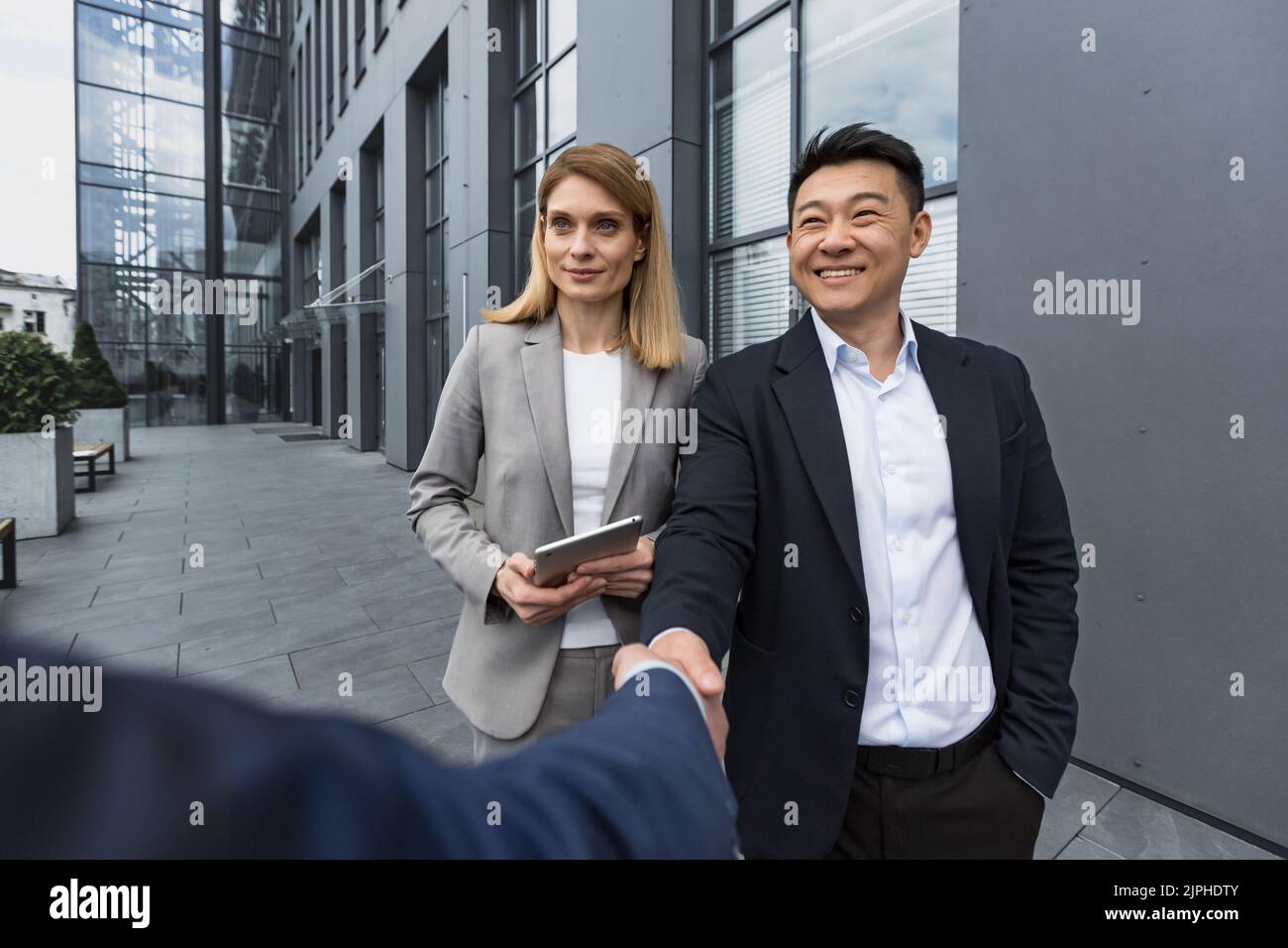 Business Meet, drei Kollegen begrüßen sich, Männer schütteln die Hände, Mitarbeiter vor dem Bürogebäude in Geschäftskleidung Stockfoto