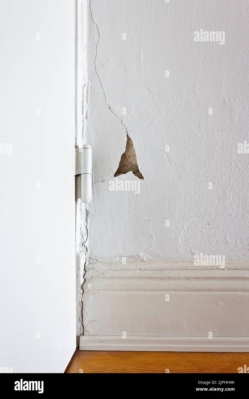 Beschädigte Eigenschaft: Weiße Wand hinter einem Türscharnier mit einem Riss oder Riss und ein Stück Gips fehlt. Sanierung des Immobilienkonzepts. Stockfoto