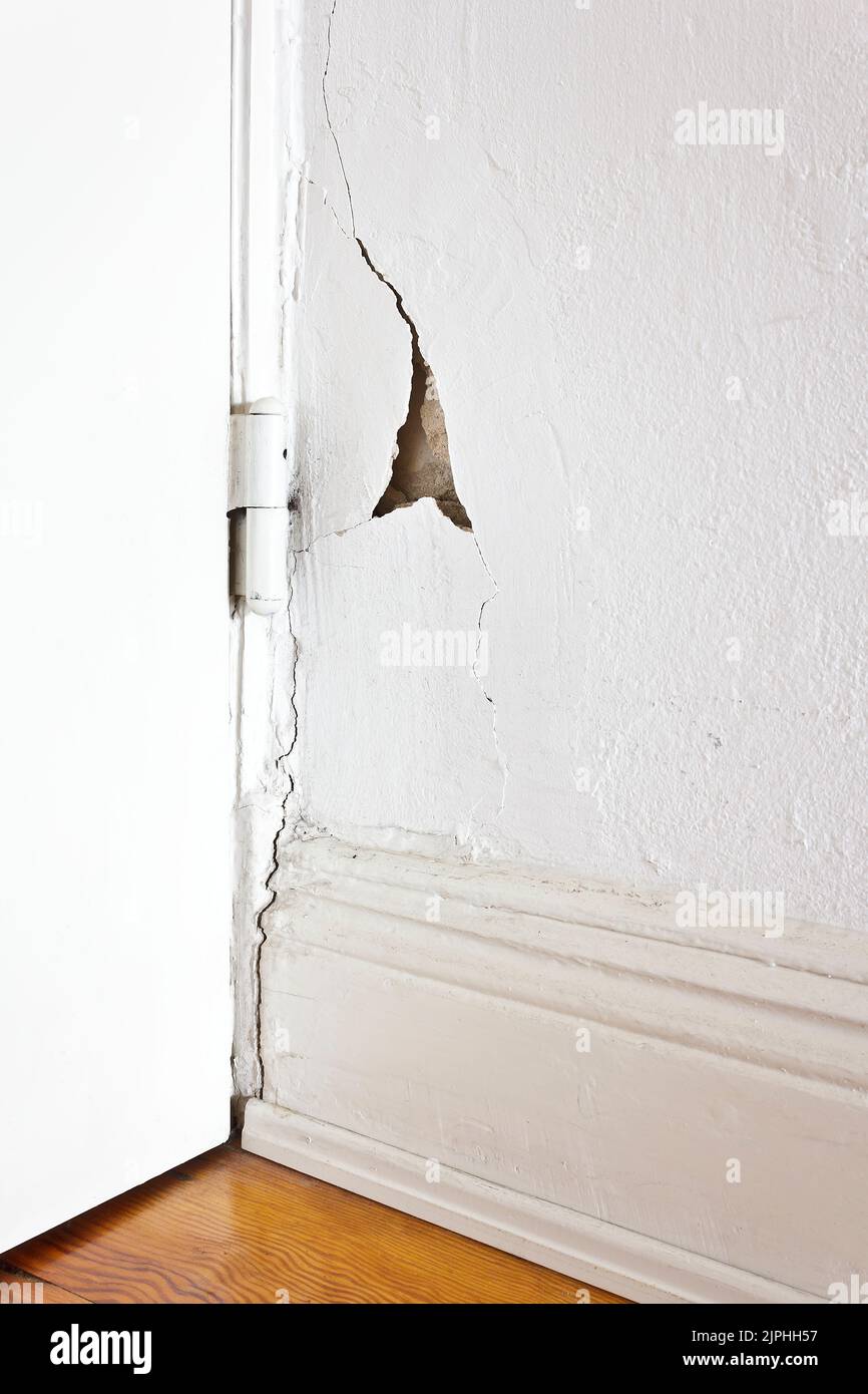 Beschädigte Eigenschaft: Weiße Wand hinter einem Türscharnier mit einem Riss oder Riss und ein Stück Gips fehlt. Sanierung des Immobilienkonzepts. Stockfoto