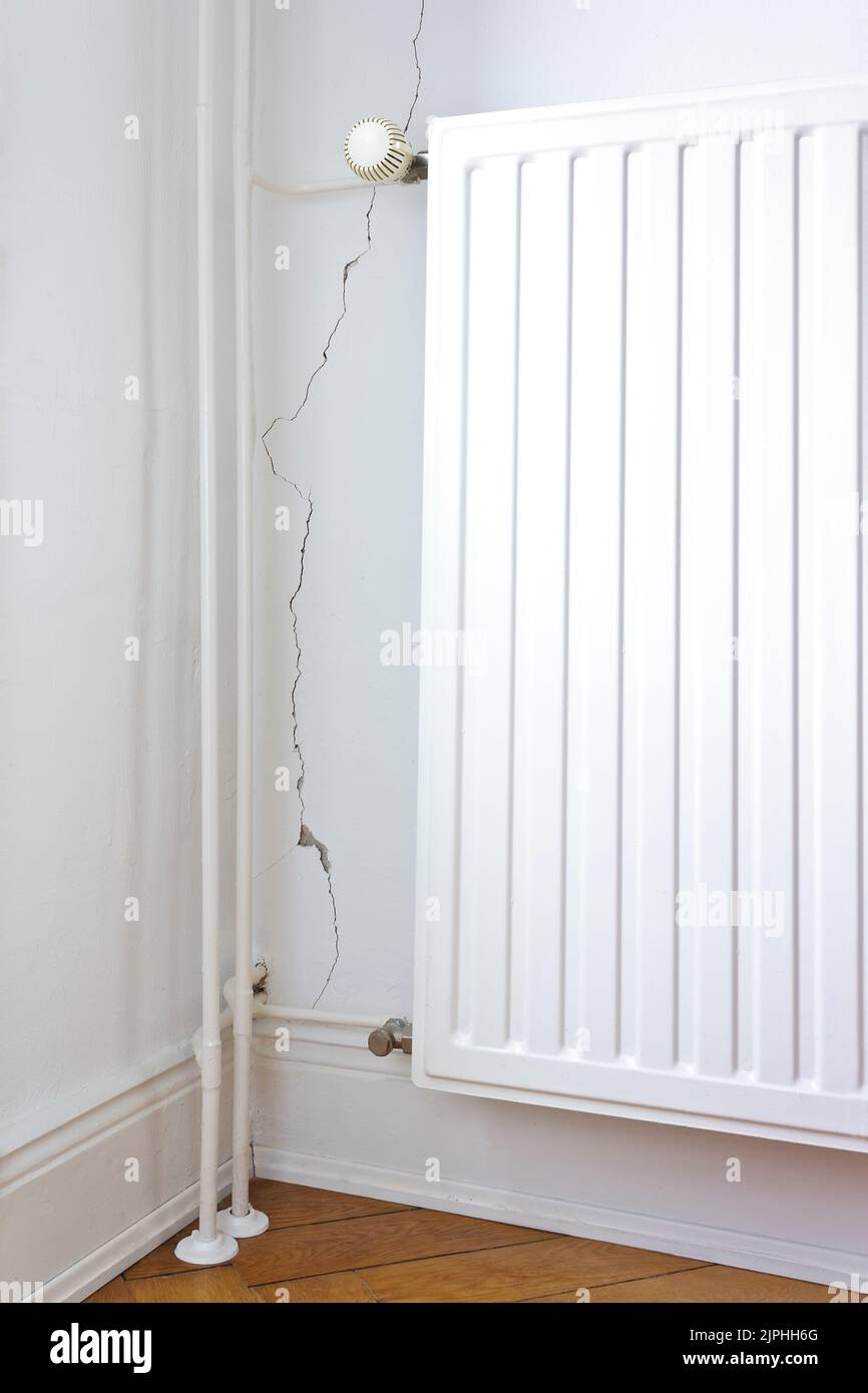Beschädigte Eigenschaft: Weiße Wand hinter einem Heizkörper oder Heizkörper mit einem Riss oder Riss und ein Stück Putz fehlt. Sanierung des Immobilienkonzepts. Stockfoto