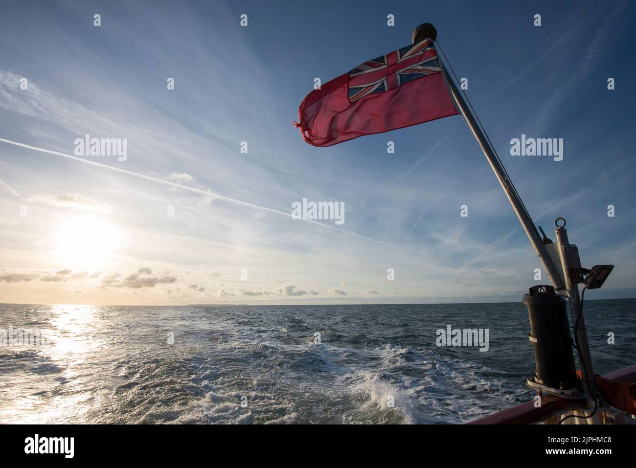 Eine nautische Flagge am Heck eines Passanten-Bootes fliegt im Wind über das Meer Stockfoto