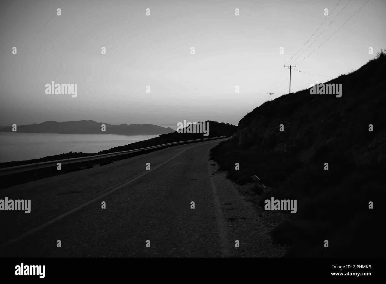 Blick auf eine einsame Straße mit atemberaubender Aussicht und einem atemberaubenden violetten Sonnenuntergang in iOS Greece in schwarz-weiß Stockfoto