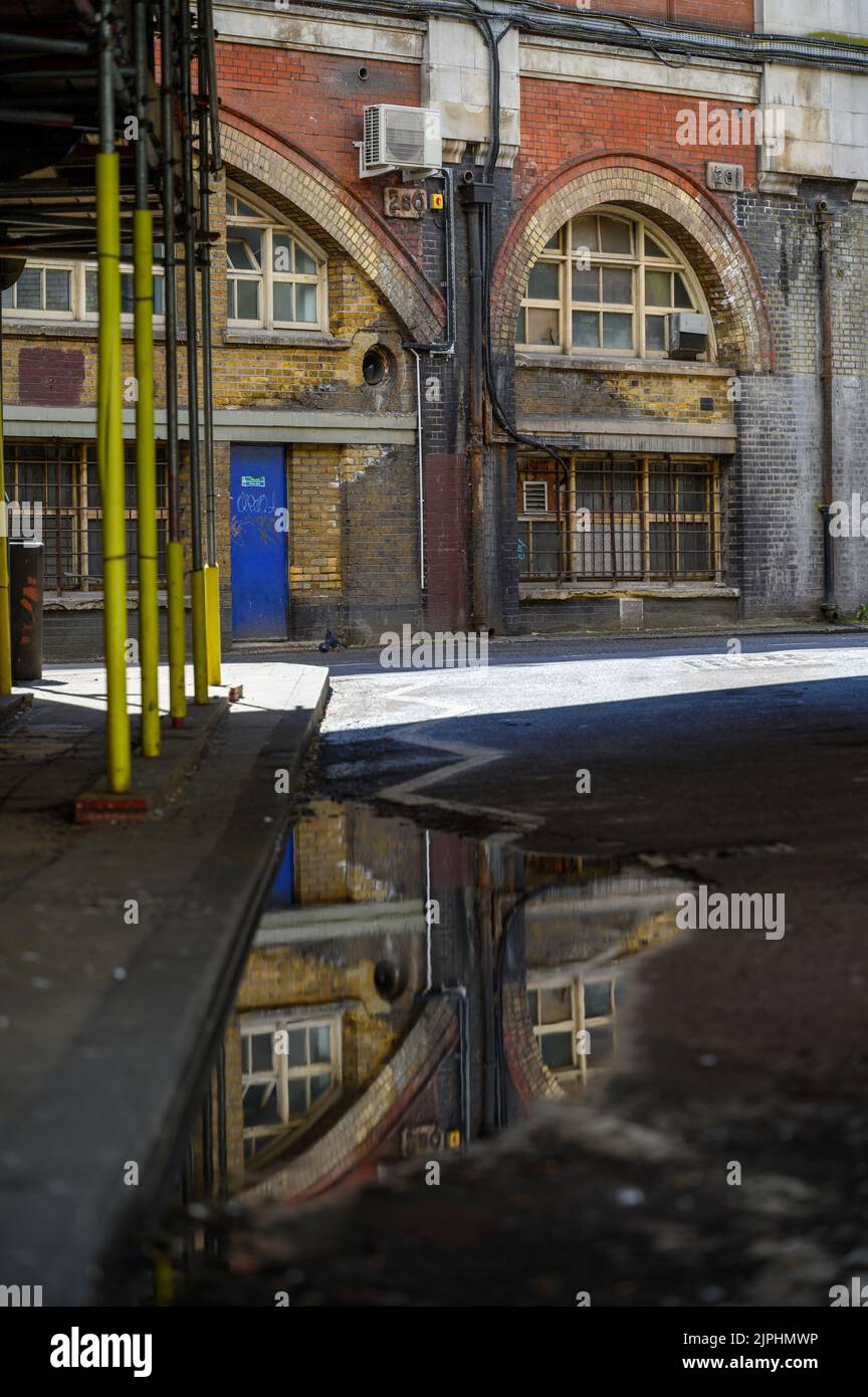 LONDON - 20. Mai 2022: Alte Backsteineisenbahn-Torbögen in Waterloo spiegeln sich in Pfützen auf der Straße wider Stockfoto