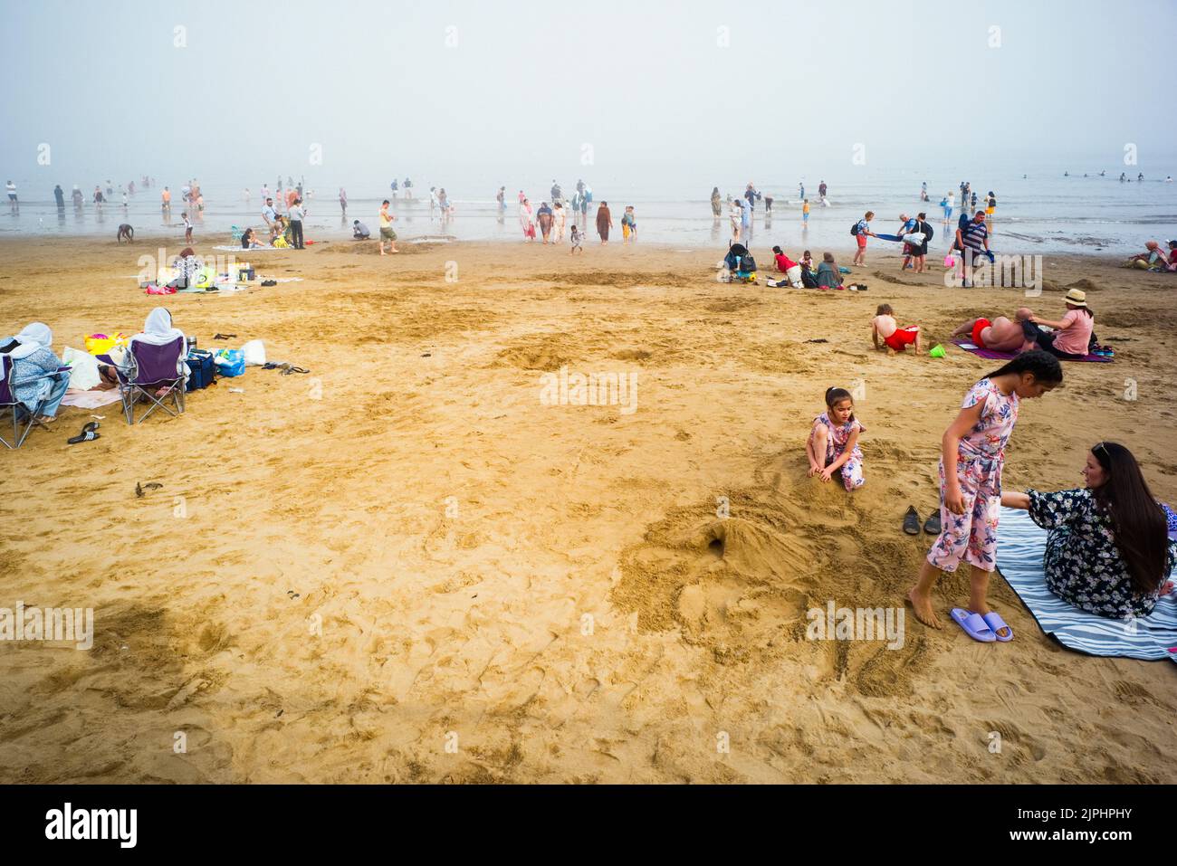 An einem Sommerwochenende ist am Strand von Scarborough viel los, mit vielen asiatischen Familien im Wasser und im Sand Stockfoto