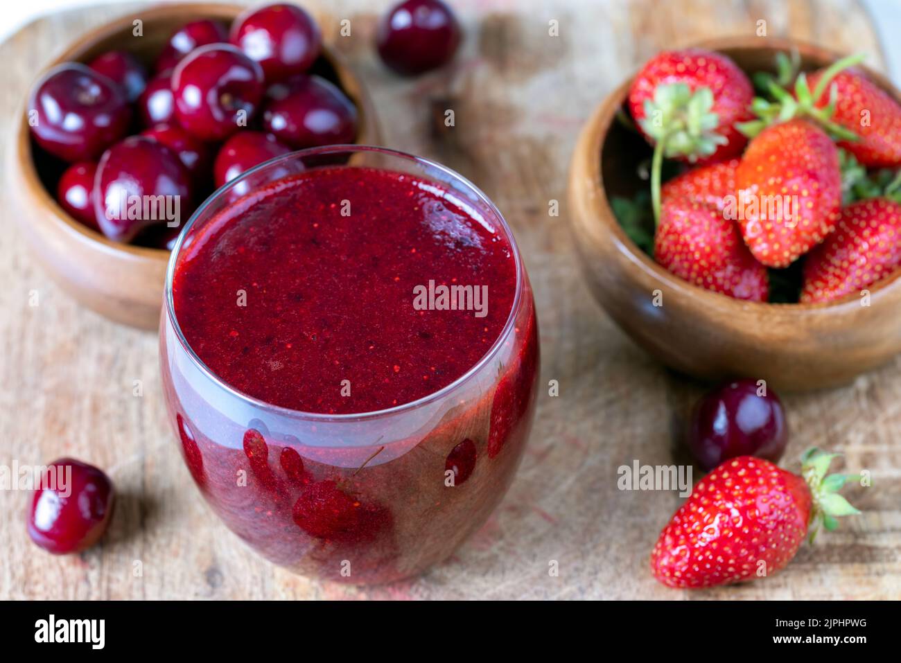 Erdbeerkirschgetränk aus zerkleinerten Beeren, gemahlenen Erdbeeren, Kirschen und Blaubeeren mit einem Mixer für die Dessertzubereitung Stockfoto