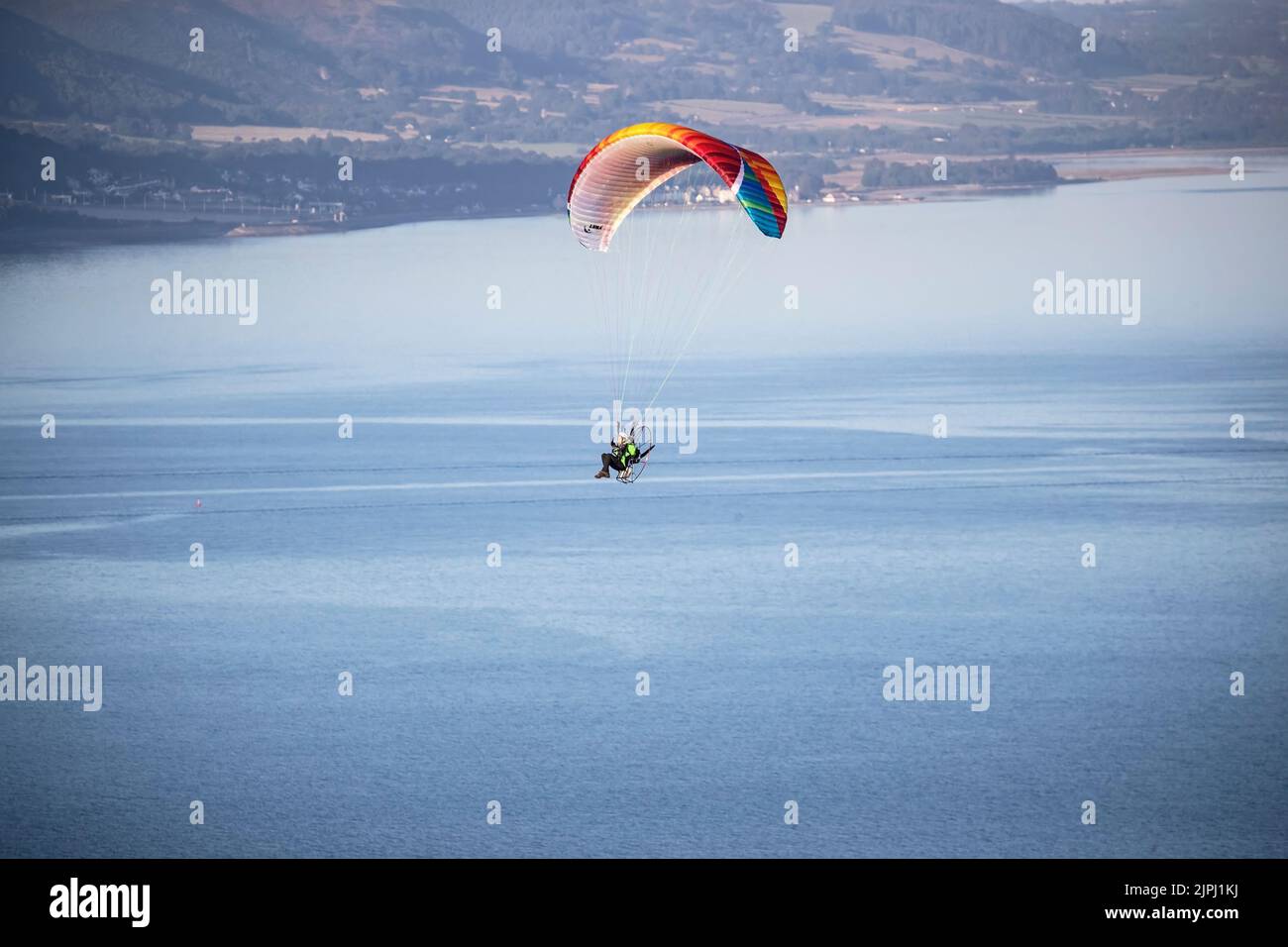 Ein Paramotor-Pilot, der an einem frühen Sommermorgen über der Mündung des Conwy River in Nordwales mit klarem blauen Himmel und einer unglaublichen Aussicht fliegt Stockfoto