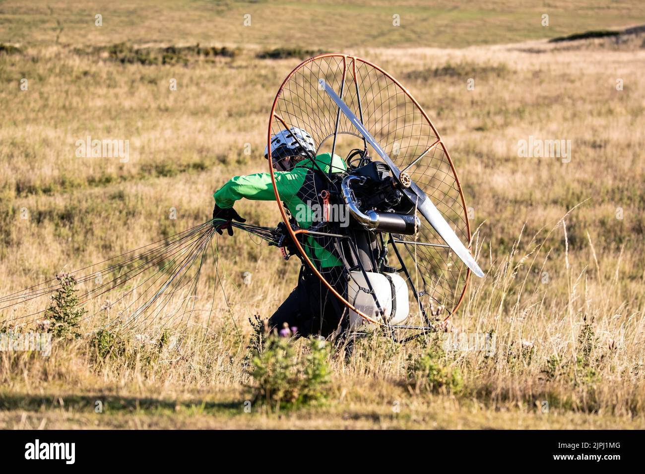 Ein Paramotor-Pilot, der sich in seinem Vordach versammelt hat, nachdem er gerade an einem frühen Sommermorgen einen allein angetriebenen Flug über der Großen Orme in Llandudno absolviert hat Stockfoto