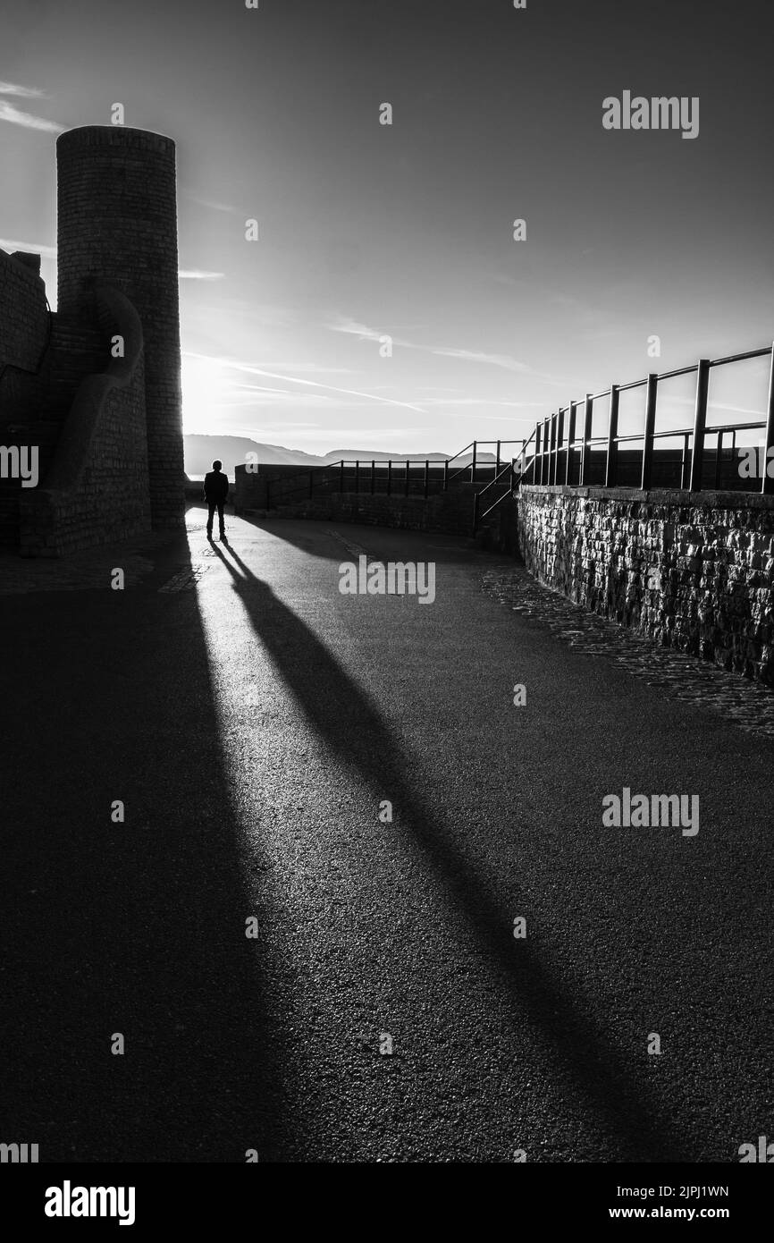 Langer Schatten eines Mannes zu Fuß in Lyme Regis, Dorset Stockfoto