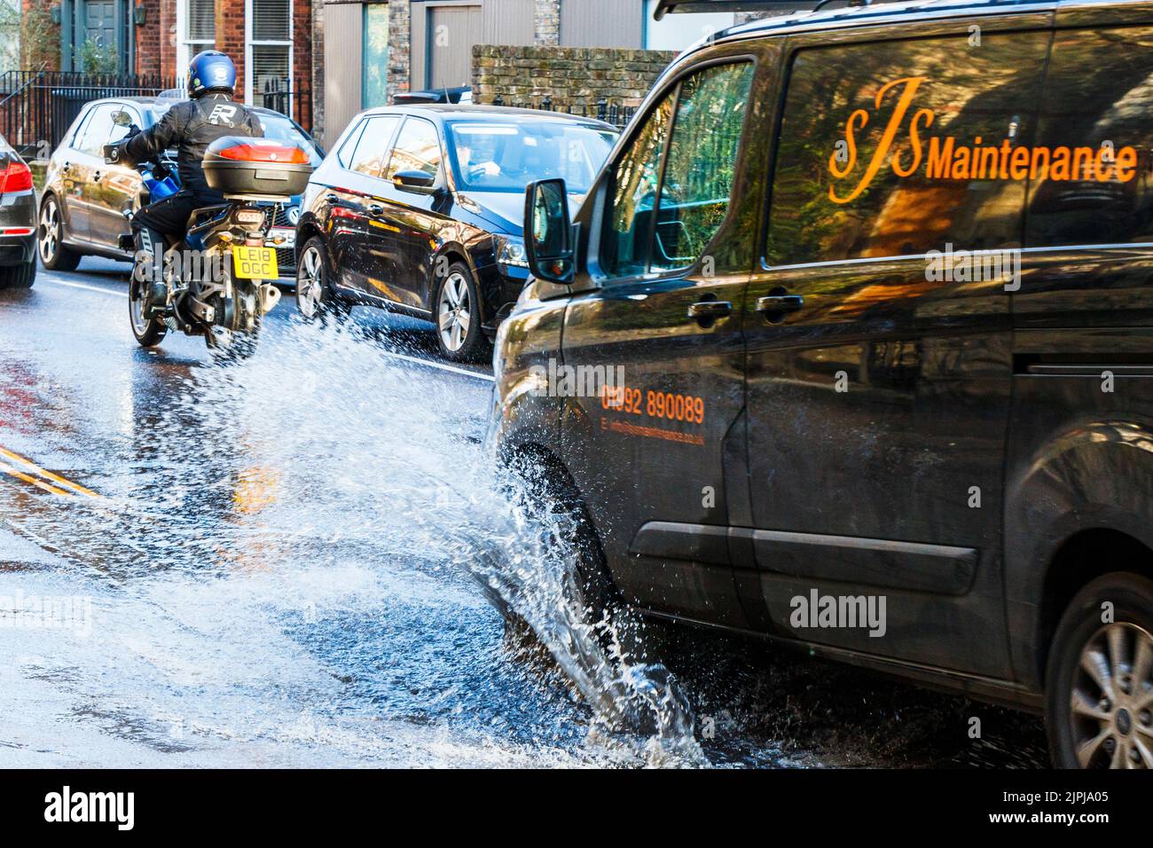 Ein Van fährt durch eine große Pfütze am Straßenrand, die durch ein Wasserleck verursacht wird, und überschüttet den Bürgersteig mit Spray, London, Großbritannien Stockfoto