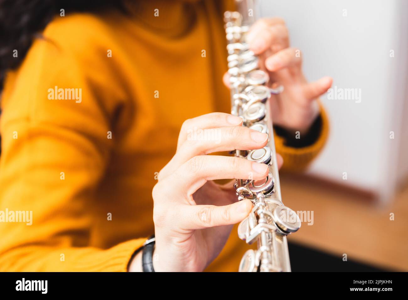 Nahaufnahme einer nicht erkennbaren Frau mit einem gelben Pullover, die eine Querflöte spielt. Stockfoto