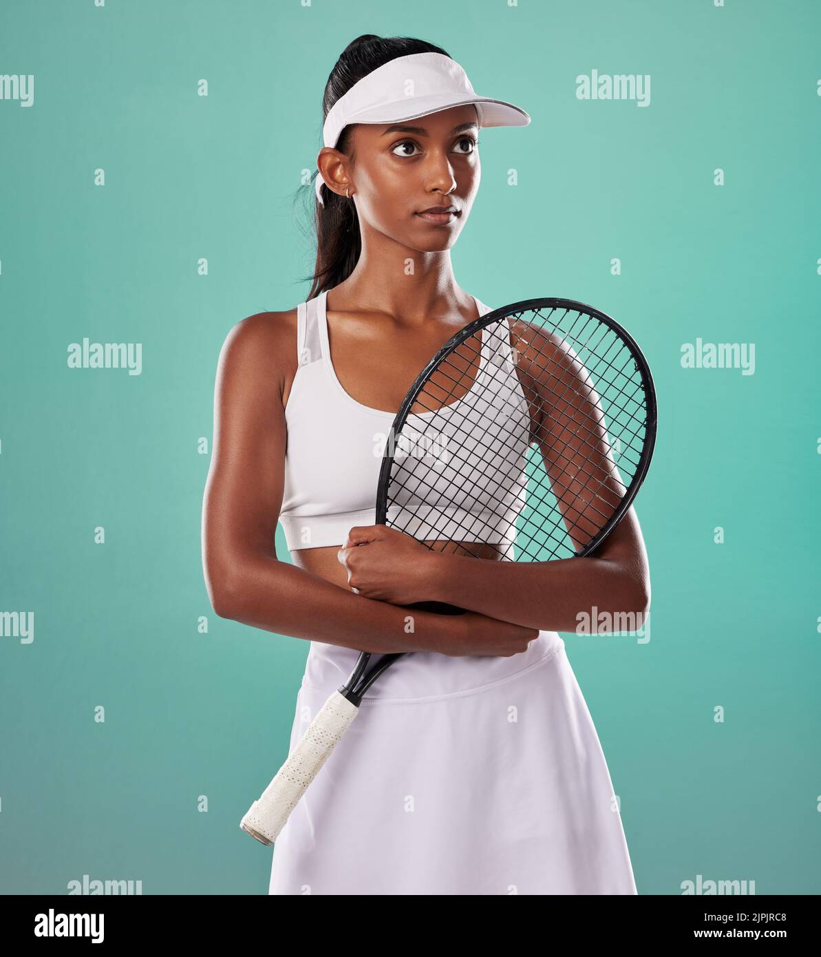 Denkende Tennisspielerin, Fitnessathletin und aktive Frau, bereit zum Training mit Schläger in cooler Mode und Sportuniform, während sie auf Grün posiert Stockfoto