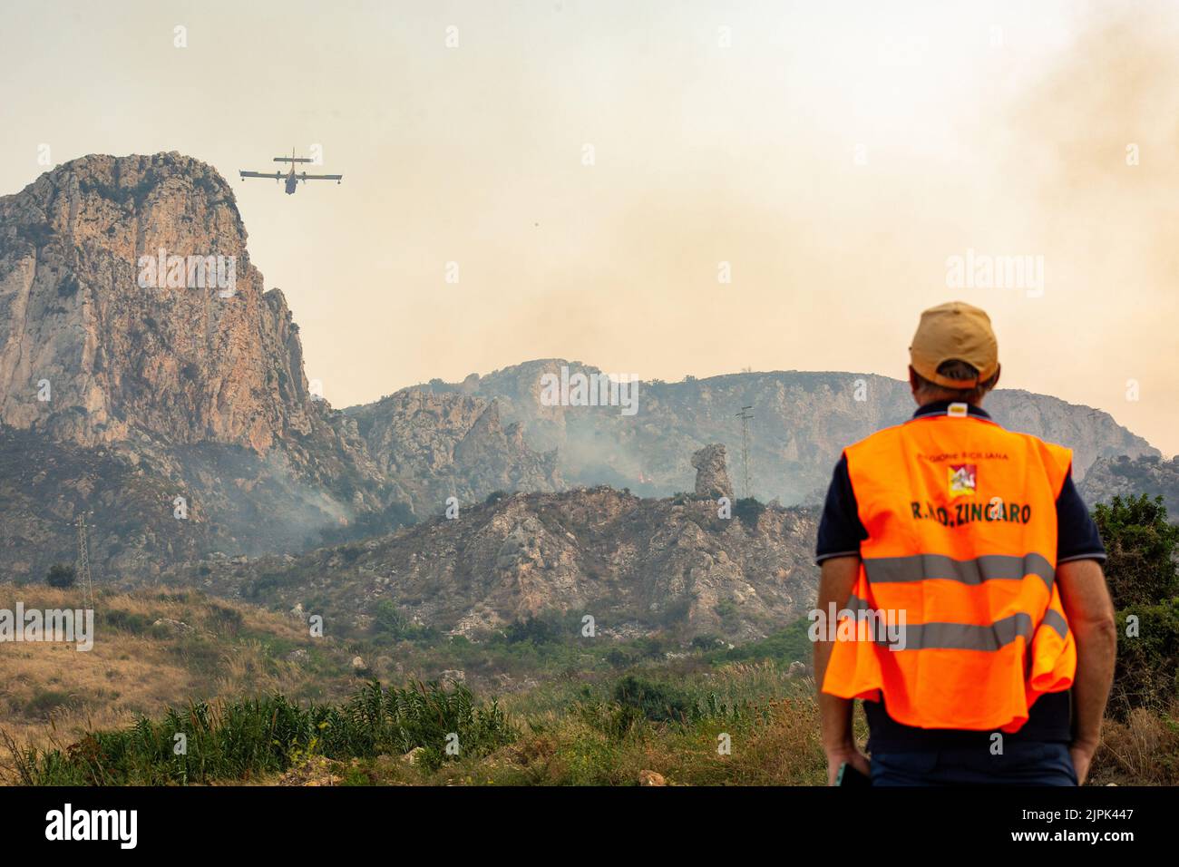 Ein Hüter des Naturreservats Zingaro beobachtet einen der Canadair in der Nähe des Reservats, in dem er arbeitet. An einem Tag mit mehr als 40 Grad Temperatur und starkem sciroco-Wind brannte ein großes Feuer fast 100 Hektar Berge in der Umgebung der Touristenstadt Scopello. Einige Häuser von Einheimischen und Touristen wurden evakuiert. Das Feuer wurde gestoppt, bevor es begann, das Naturschutzgebiet Zingaro zu verbrennen, das erste, das 1981 auf Sizilien ausgerufen wurde. Zwei Canadair, zwei Hubschrauber, einer von der Waldwache und einer von der Armee, zusammen mit mehreren Waldwächter-Landgruppen gelang es, s zu erreichen Stockfoto