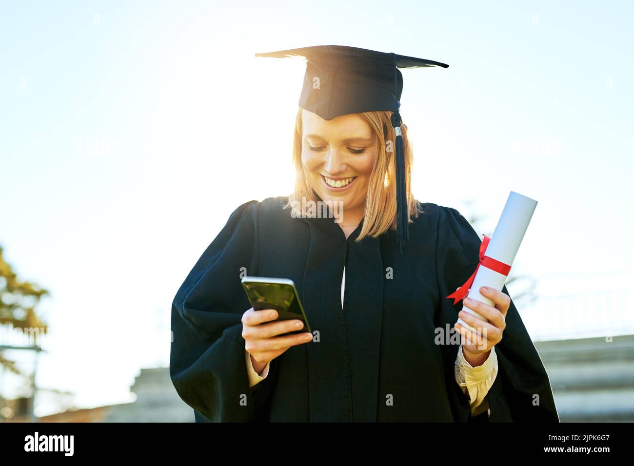 Der schnellste Weg, um allen von ihrem großen Tag zu erzählen. Studentin benutzt ihr Handy am Abschlusstag. Stockfoto