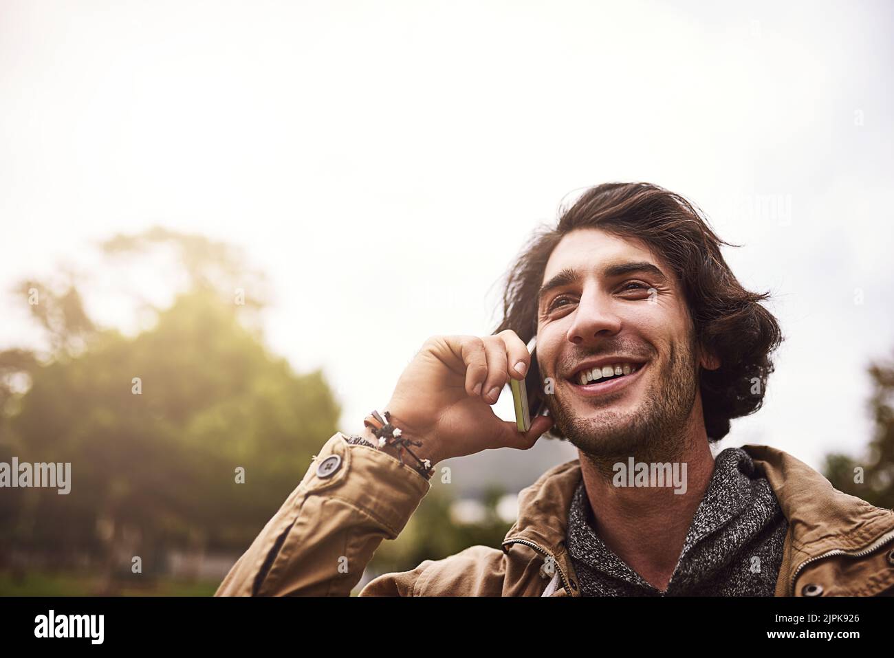 Ich bin so froh, dass Sie. Ein fröhlicher junger Mann, der am Telefon spricht, während er draußen in einem Park steht. Stockfoto