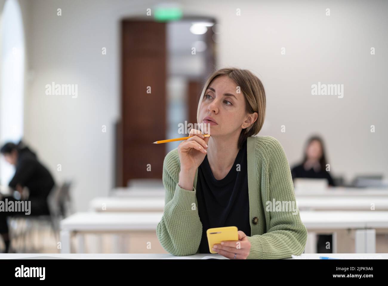 Nachdenkliche Frau reifer Student Blick in die Ferne während des Studiums in der Bibliothek, desinteressiert an Studie Stockfoto