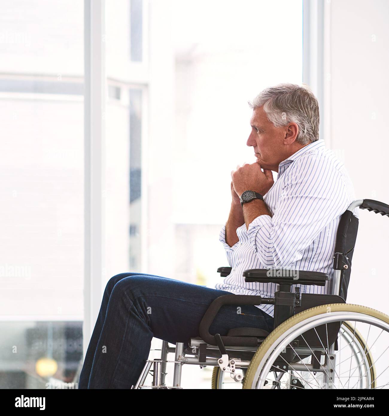 Es geht ihm viel durch den Kopf. Ein fokussierter reifer Mann sitzt in einem Rollstuhl, während er in einer Klinik nachdenkt. Stockfoto