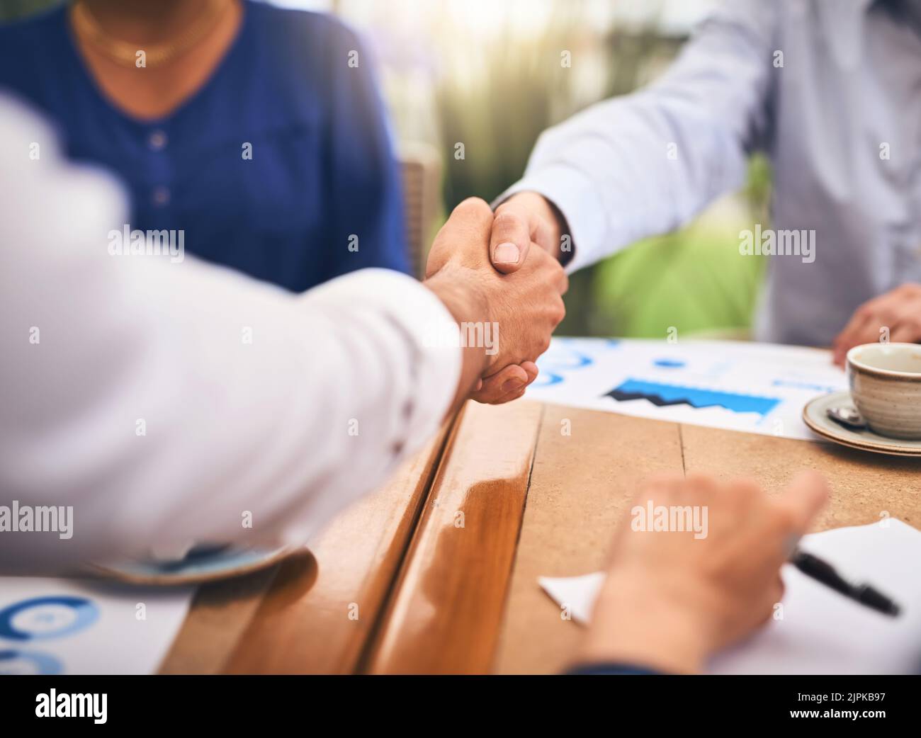 Ich bin froh, dass wir uns darüber einig sind: Zwei unkenntliche Geschäftsleute, die sich einig über einen Tisch in einem Coffeeshop die Hände schütteln. Stockfoto