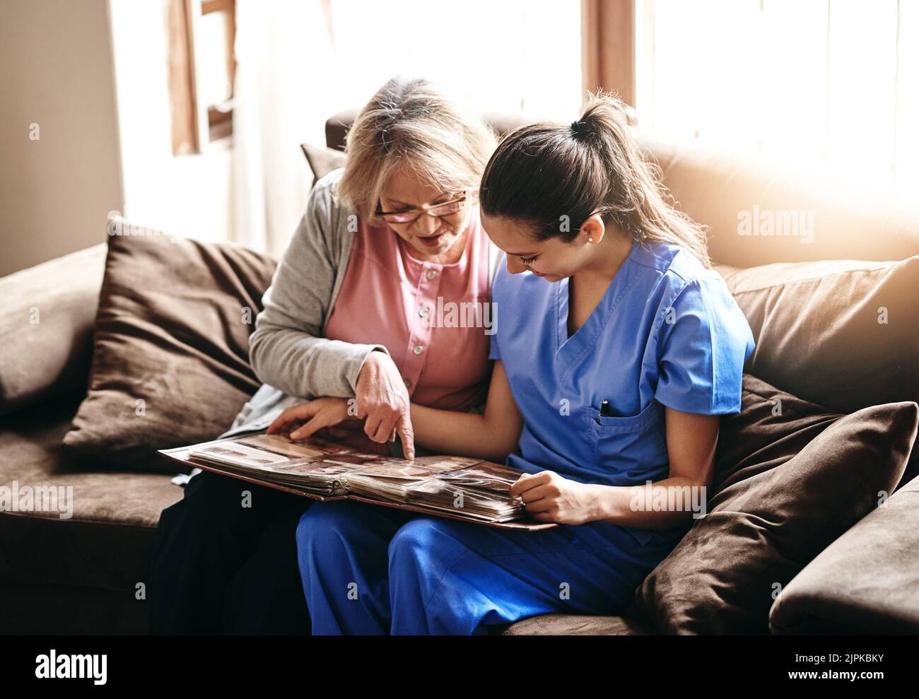 Eine Krankenschwester und eine ältere Frau betrachten zusammen ein Fotoalbum. Stockfoto