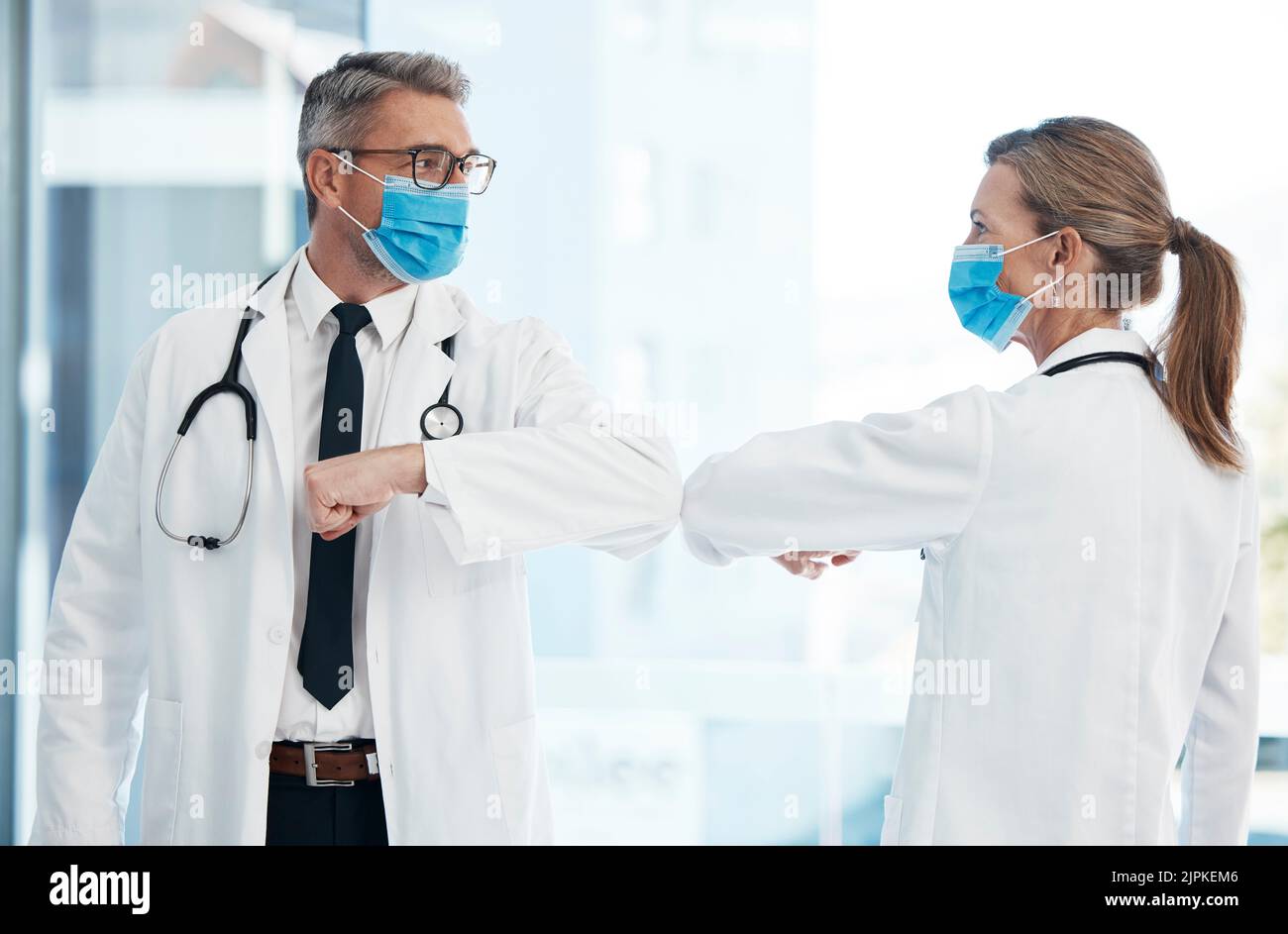 Ärzte tun covid sichere Begrüßung mit Ellbogen, tragen Gesichtsmaske, um vor Viren zu schützen und arbeiten in einem Krankenhaus. Pflegekräfte sprechen in einer Klinik Stockfoto