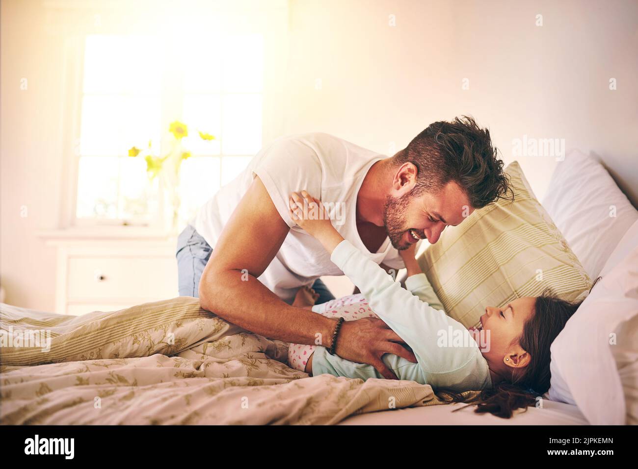 Verspielte Albernheit zu Hause. Ein fröhlicher Vater und eine fröhliche Tochter, die zu Hause auf dem Bett kitzeln. Stockfoto