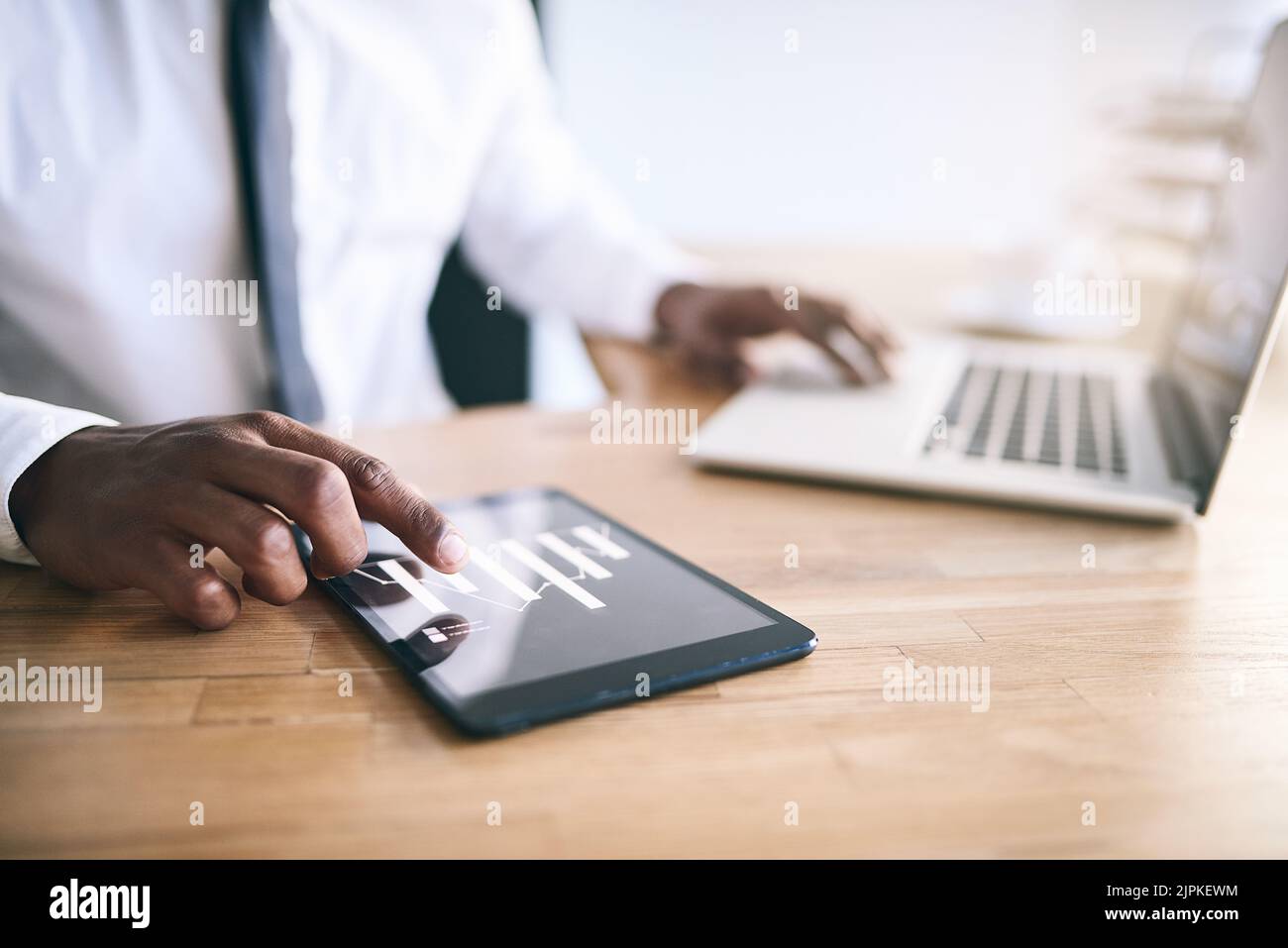 Digitales Multitasking. Ein nicht erkennbarer Geschäftsmensch, der auf einem Laptop tippt, während er auch ein Tablet benutzt. Stockfoto