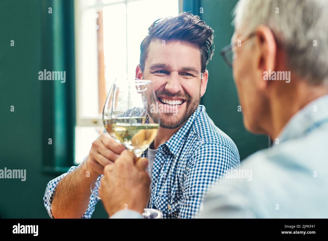 Ein fröhlicher junger Mann und sein reifer Vater teilen sich zu Hause einen feierlichen Toast mit Weingläsern. Stockfoto
