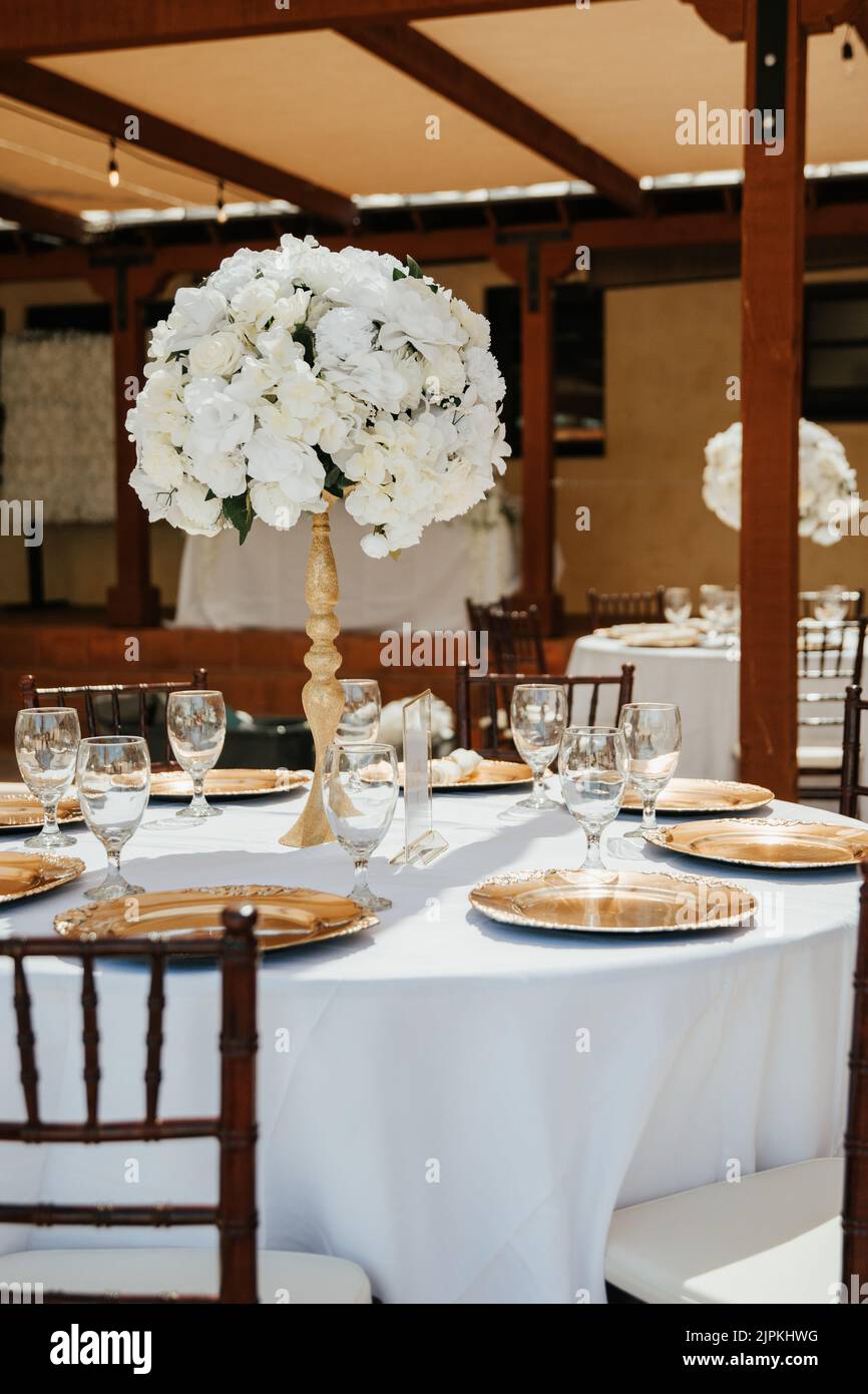 Wunderschöne Außenrezeptionsstätte - weiße Tischdecken, goldene Teller, weiße Rosen in den Mittelpunkt Stockfoto