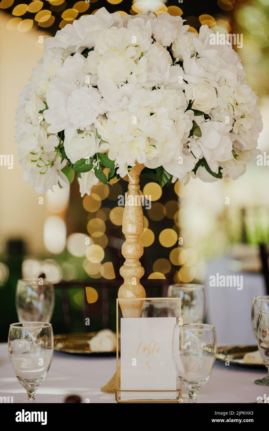 Wunderschöne Außenrezeptionsstätte - weiße Tischdecken, goldene Teller, weiße Rosen in den Mittelpunkt Stockfoto
