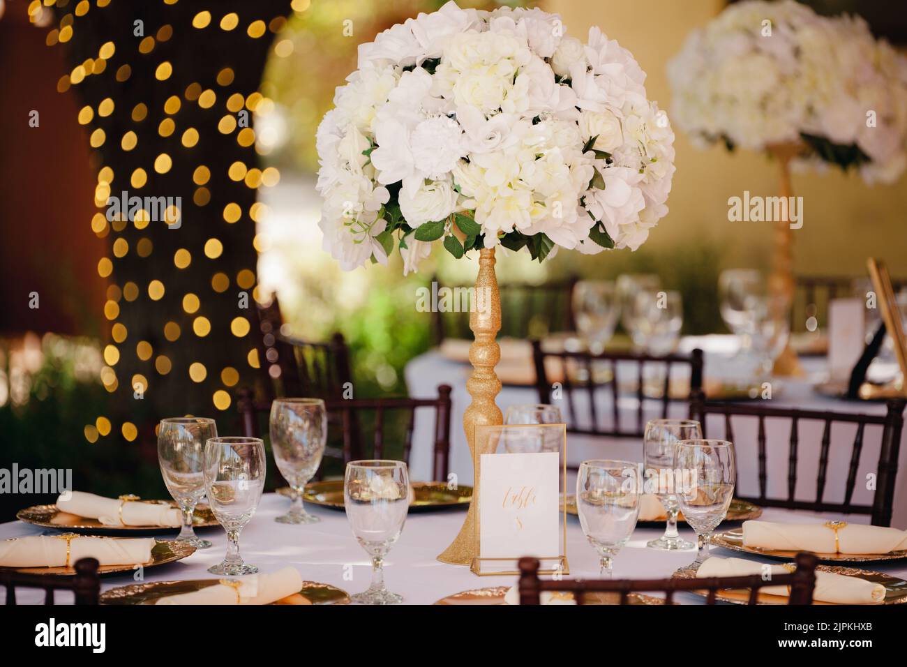 Wunderschöne Außenrezeptionsstätte - weiße Tischdecken, goldene Teller, weiße Rosen in den Mittelpunkt Stockfoto