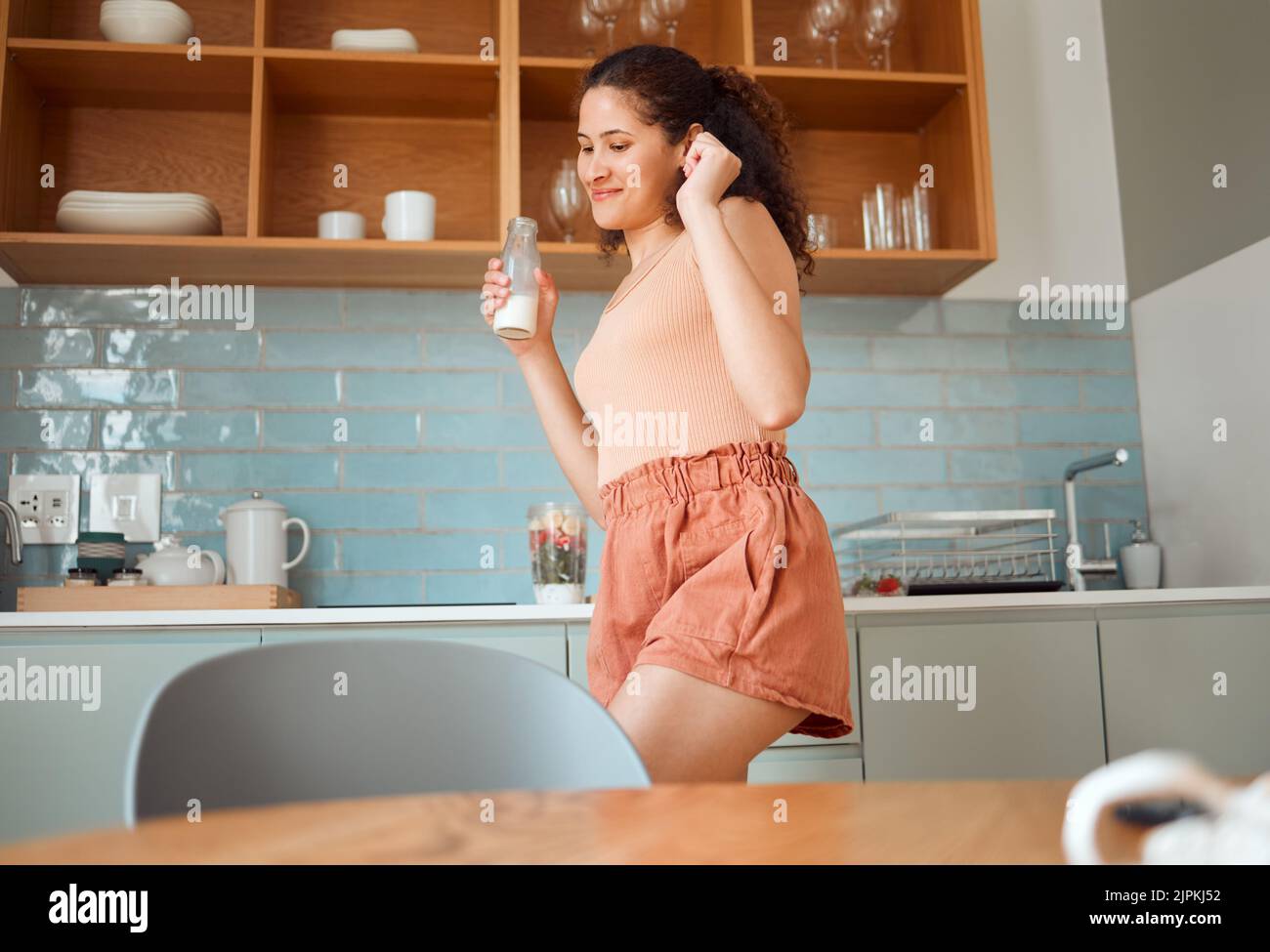 Verspielte, fröhliche und fröhliche Frau, die tanzt und den Morgen in der Küche genießt, während sie Milch trinkt. Aufgeregte lateinische Frau, die Spaß hat Stockfoto