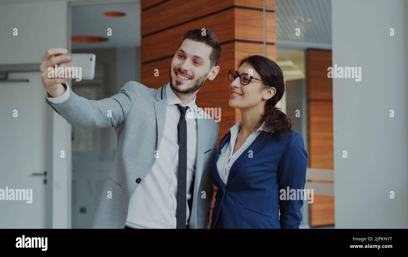 Glücklicher Geschäftsmann und seine Kollegin machen ein Selfie auf einer Smartphone-Kamera für Social Media in modernen Büroräumen Stockfoto