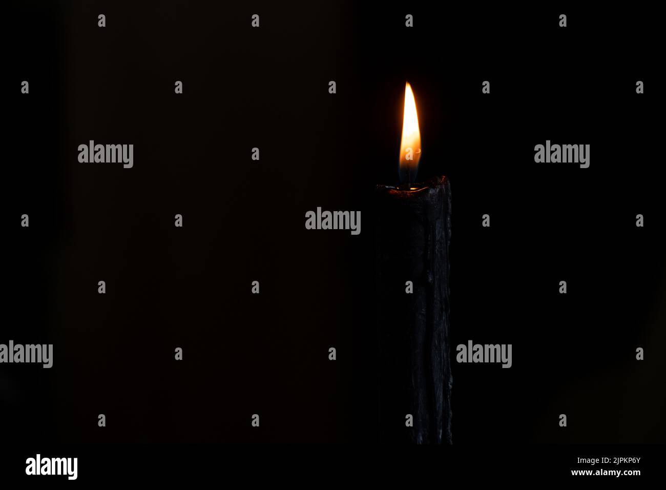 Die Flamme einer schwarzen Kerze im Dunkeln, die um die Toten und die Religion trauert Stockfoto