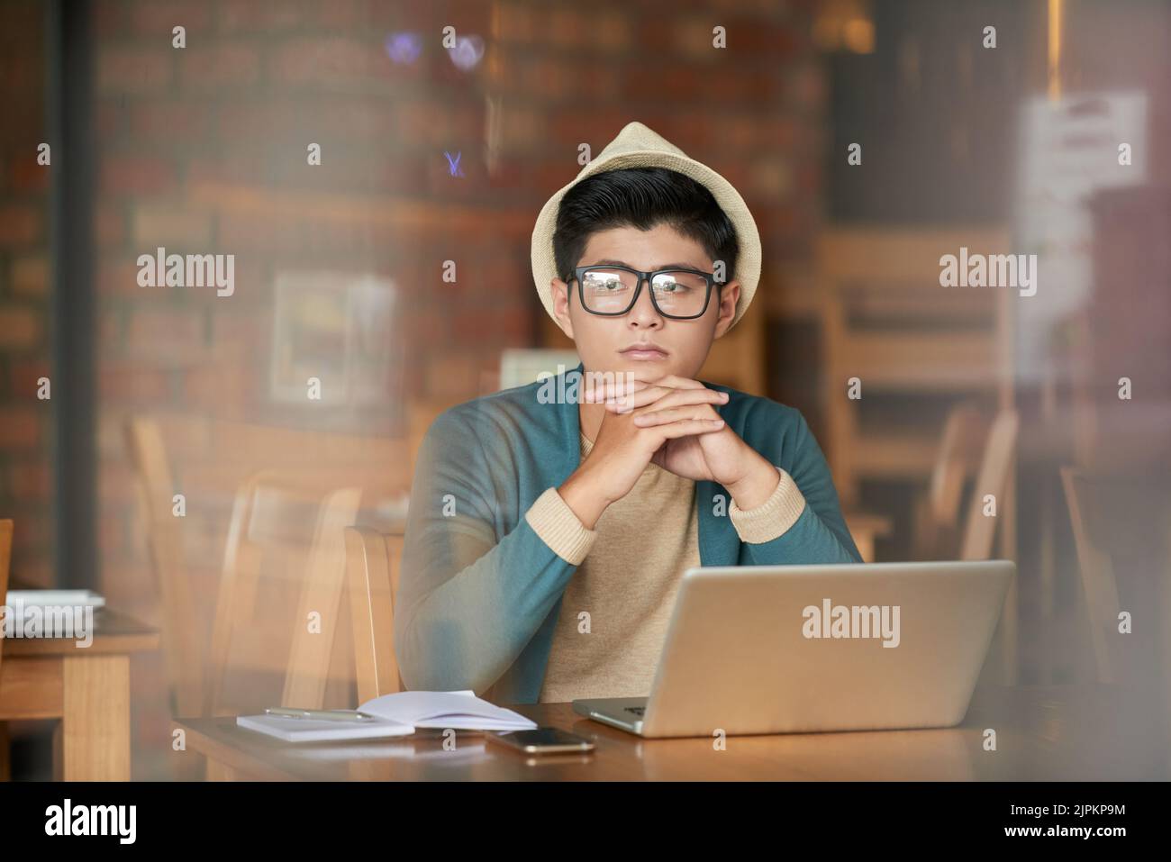 Nachdenklicher, kreativer vietnamesischer junger Mann, der in einem Café sitzt Stockfoto