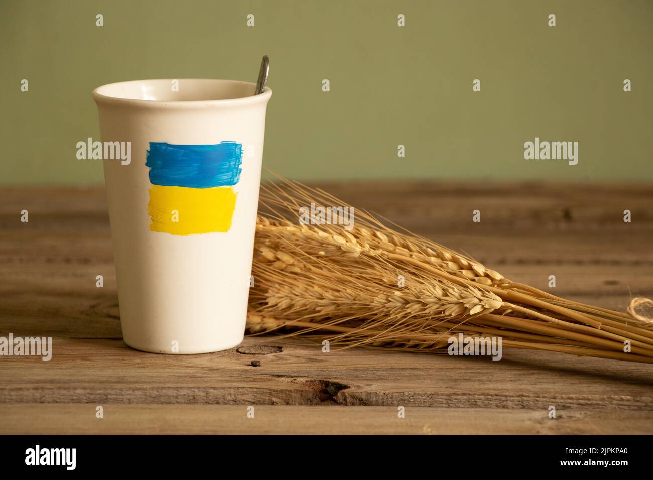 Die gelb-blaue Flagge der Ukraine ist auf einer weißen Tasse mit Kaffee auf dem Tisch in der Nähe des Weizenfeldes in der Ukraine gemalt, den Krieg zu stoppen Stockfoto