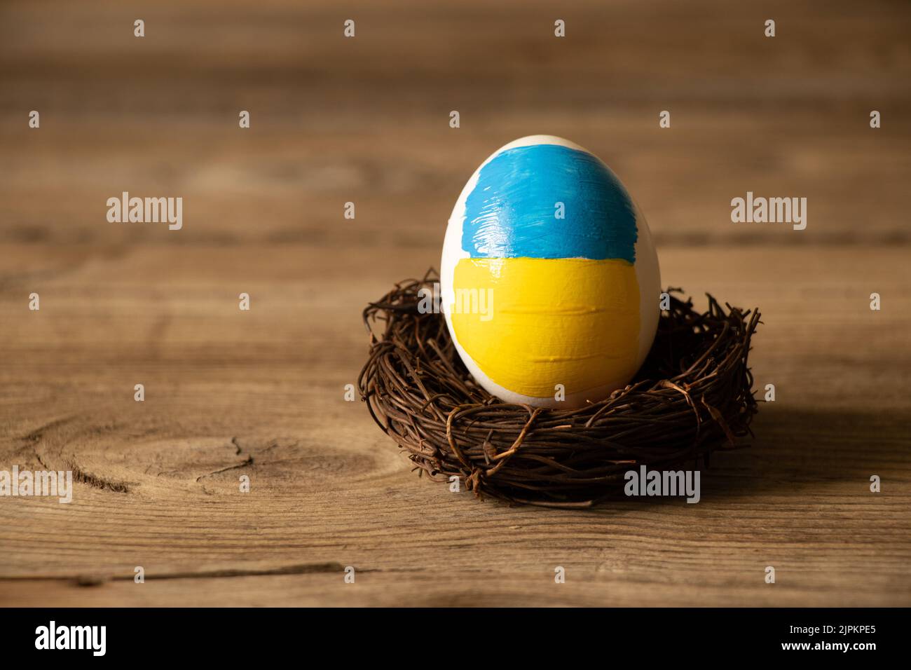 Ein weißes Hühnerei mit einer bemalten Flagge der Ukraine in einem Strohkorb auf dem Tisch zu Hause, Kultur und Urlaub 2022 Stockfoto