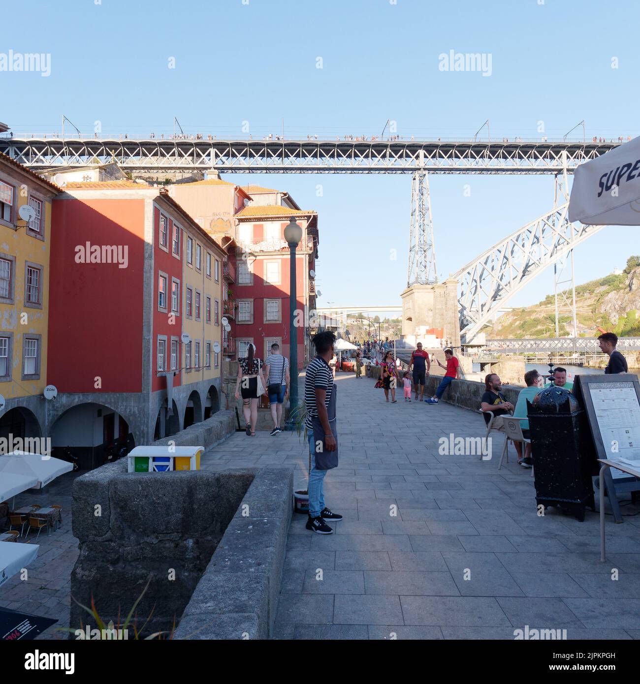 Gäste speisen in einem Restaurant im Ribeira aka Riverside Viertel von Porto mit einem Restaurantmitarbeiter im Vordergrund und der Luis I Brücke im Hintergrund. Stockfoto