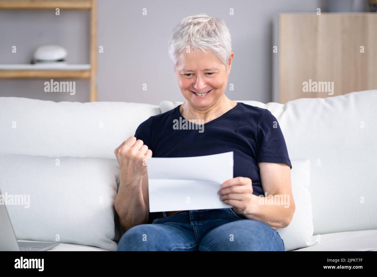 Lächelnde Frau Beim Lesen Des Briefes, Während Sie Zu Hause Auf Dem Sofa Sitzt Stockfoto