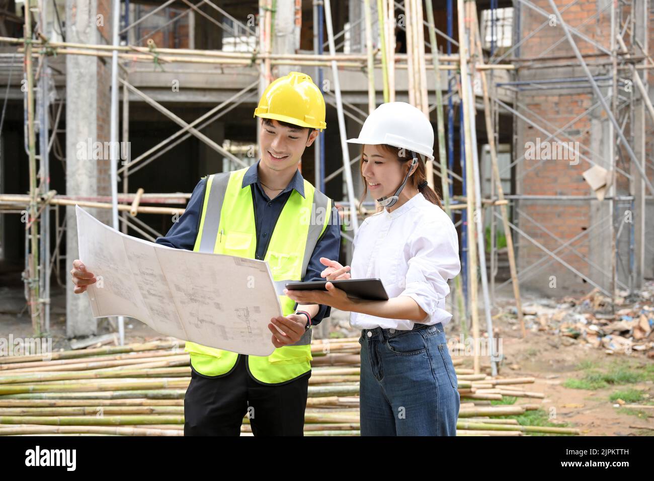 Schöne und talentierte junge asiatische Frau Bauingenieurin Blick auf die Blaupause während der Diskussion mit einem professionellen männlichen Bauinspektor an Stockfoto