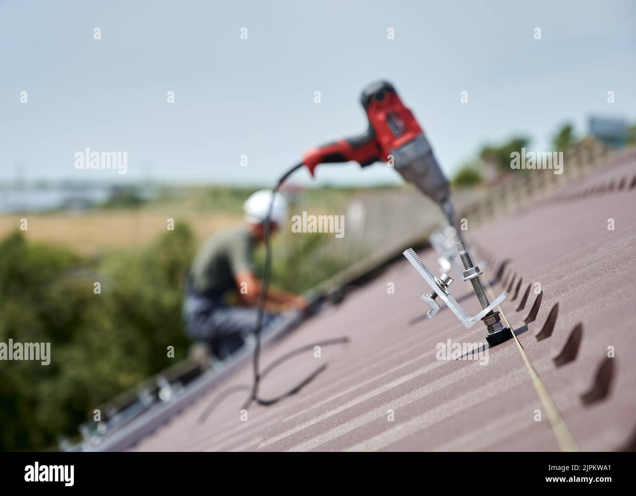 Nahaufnahme der Klemme. Arbeiter Vorbereitung auf die Installation von Photovoltaik-Solarpanel-System auf dem Dach des Hauses. Mann und elektrischer Schraubendreher auf unscharfem Hintergrund. Stockfoto
